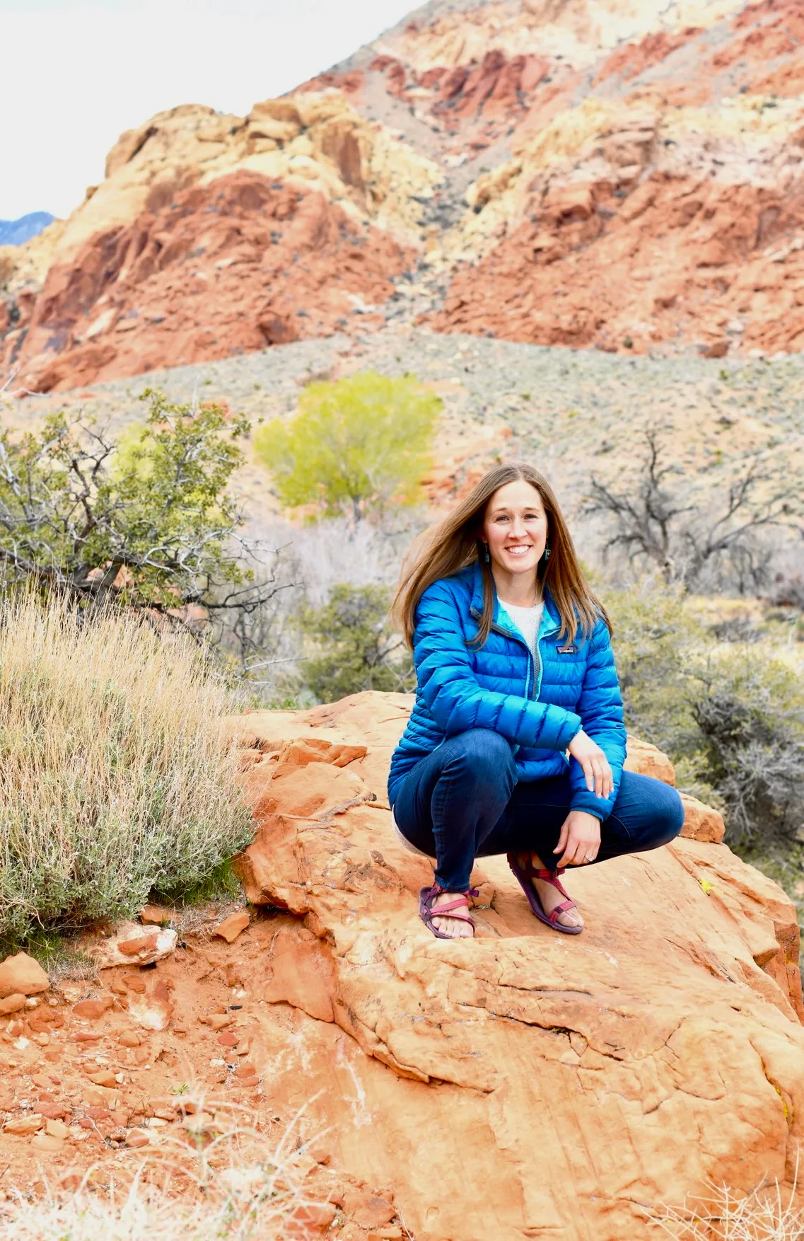 Adrienne sitting on red sandstone among desert scrub and mountains